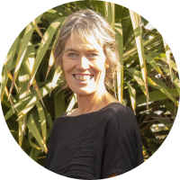 Head and shoulders photo of Jackie Burrow, who is standing in front of a flax bush.